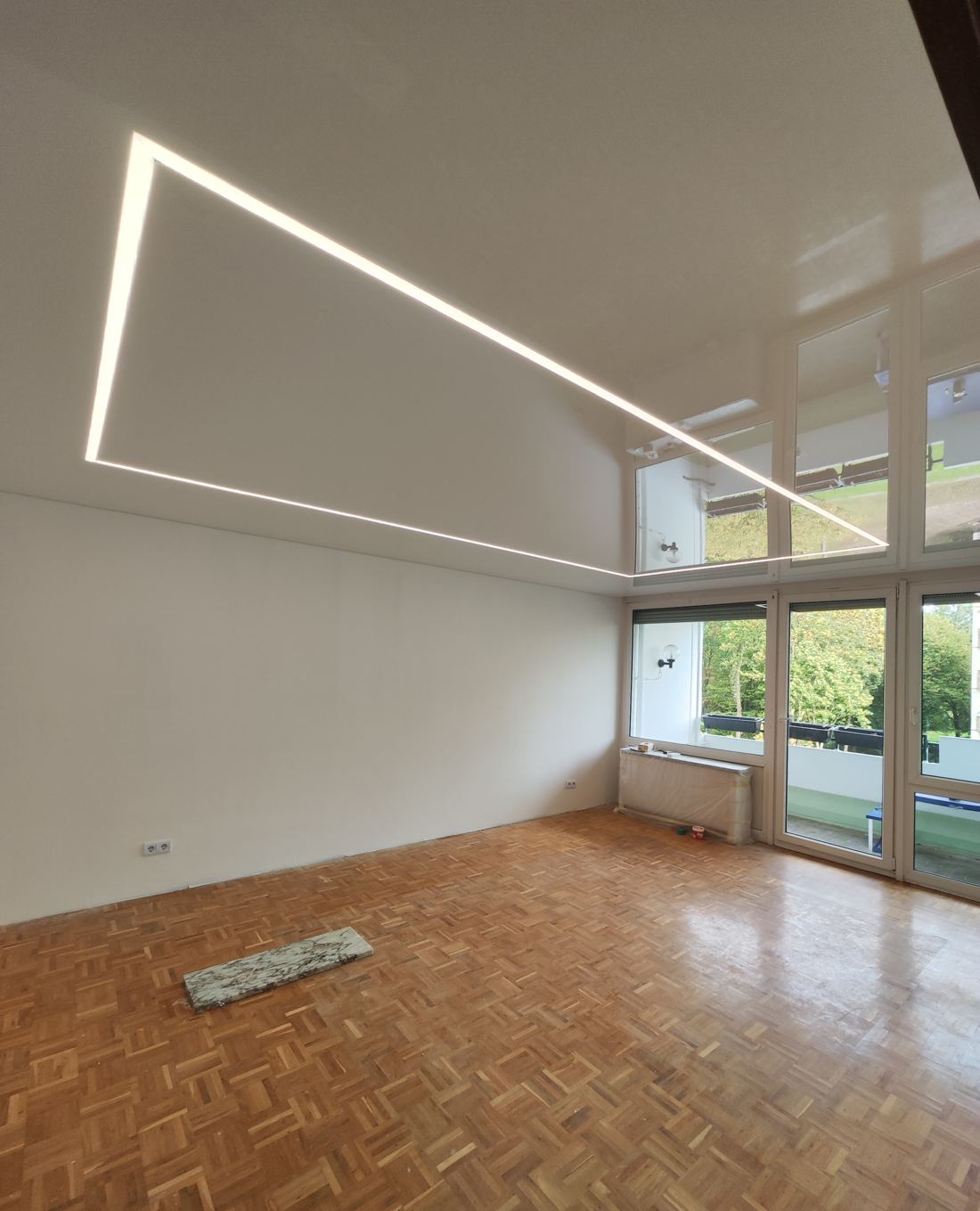 Wohnraum mit glänzender Spanndecke und winkligen LED-Lichtlinien